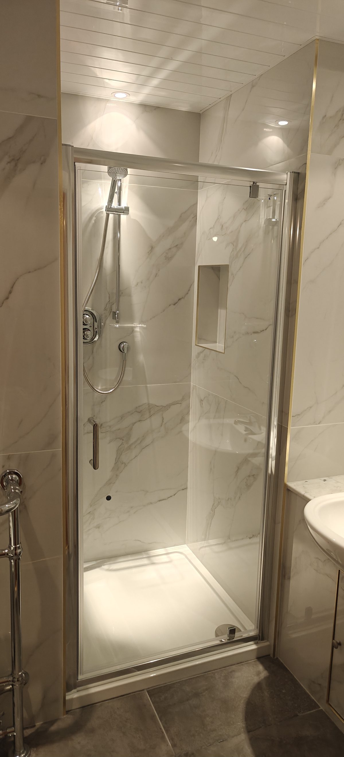 Walk-in shower with brass trim and large format marble effect tiles